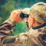 A hunter holding a pair of high-quality binoculars in the woods.